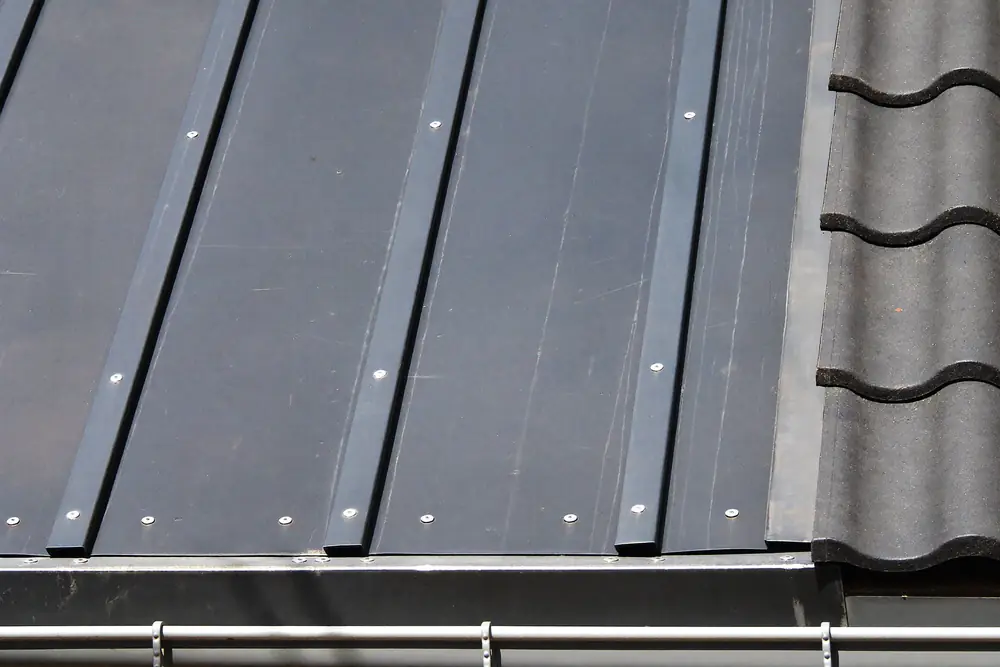 Donkergrijze strokenbekleding naast dakpannen met een nette afwerkrand, zoals op de wang van een dakkapel