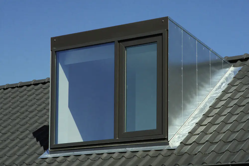 Moderne dakkapel met slanke donkere aluminium kozijnen, grote ramen en zinken wangen op een antracietkleurig dak