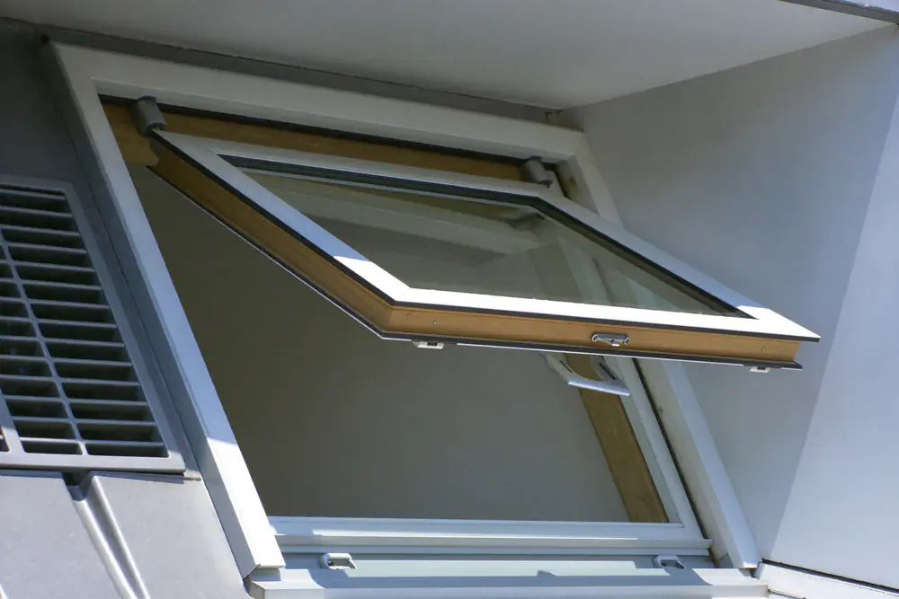 Een draaikiepraam in een dakkapel staat in kiepstand open, met een ventilatierooster ernaast