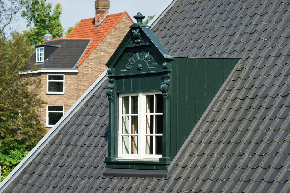 Houten dakkapel in donkergroen met witte kozijnen en fijne houtdetails op een pannendak