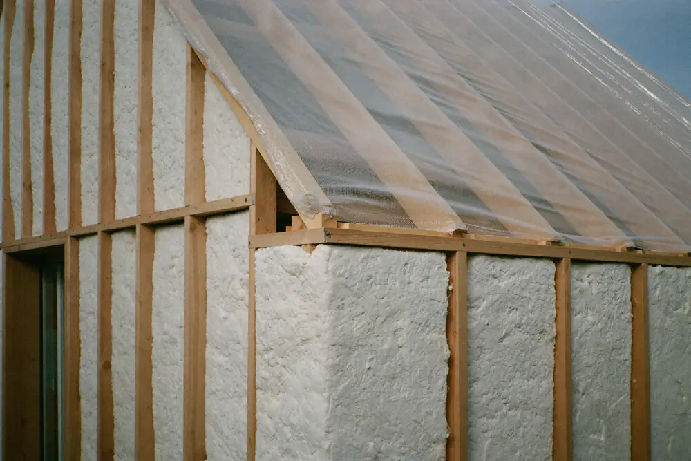 Isolatie tussen houten stijlen in de wand van een dakkapel tijdens de bouw, met een dampremmende folie op het dak