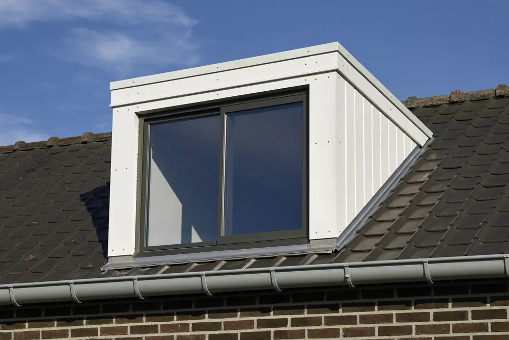 Witte kunststof dakkapel met antracietkleurige kozijnen op een donker pannendak boven een bakstenen gevel