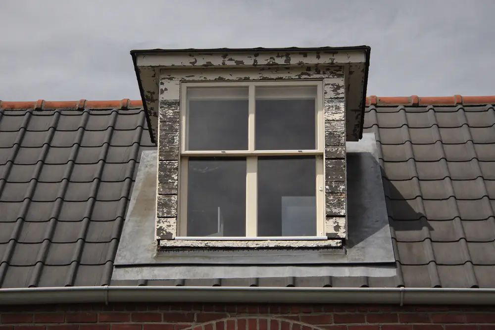 Oude dakkapel met afbladderende verf en verweerd houtwerk op een pannendak