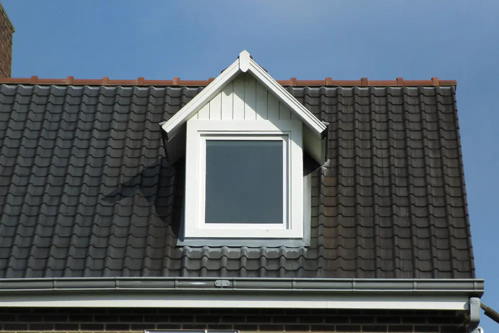 Dakkapel met een eigen puntdak en een witte houten voorkant op een donker pannendak