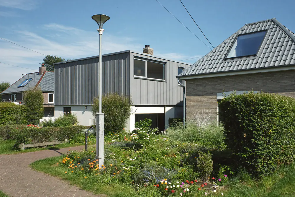 Hoekwoning met een zijtuin, een dakraam en een grijs gevelvolume, naast een lantaarnpaal en een heg