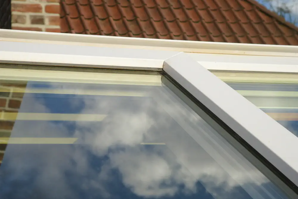 Close-up van het witte kozijn en de dubbele beglazing van een dakkapel met wolken in het glas