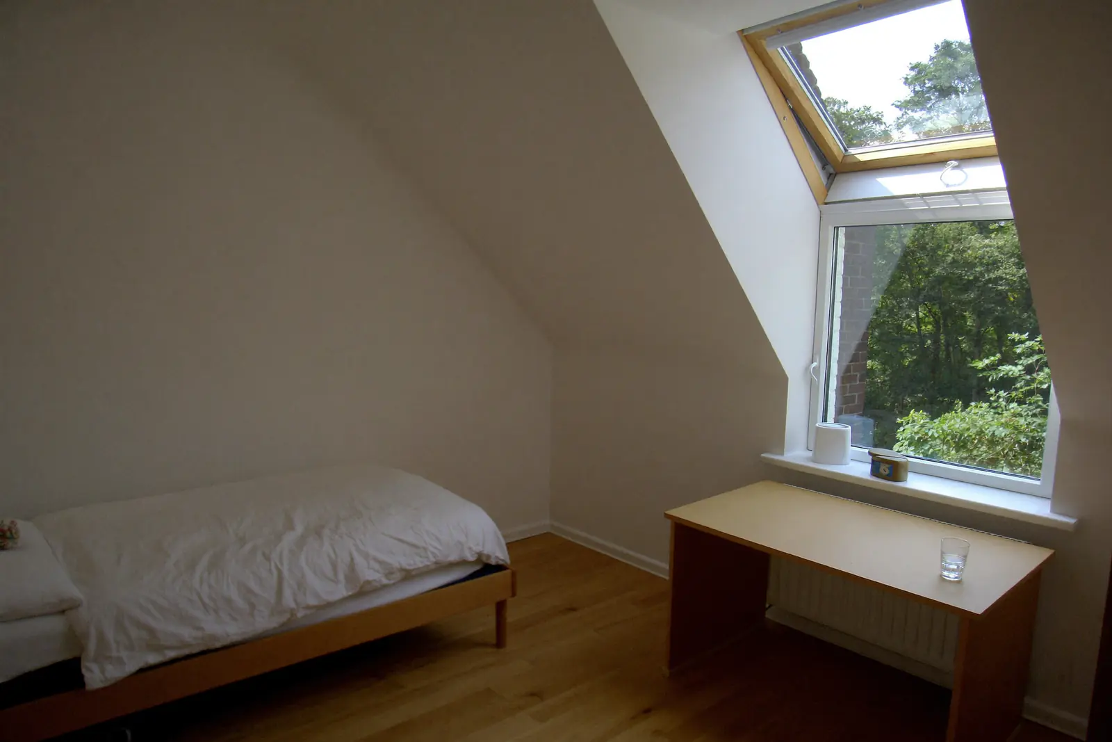 Zolderkamer met een eenpersoonsbed, een bureau en een groot raam in het schuine dak